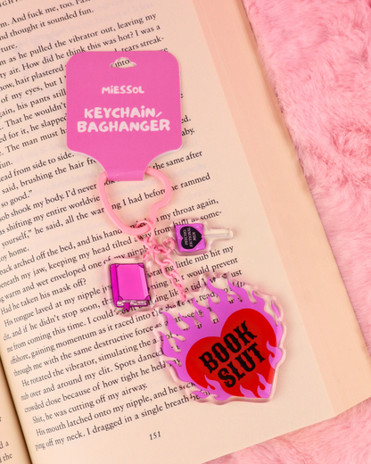 Pink and red Book Slut keychain with heart-shaped hardware and three bookish charms, a funny book lover accessory for bags, keys and book sleeves.