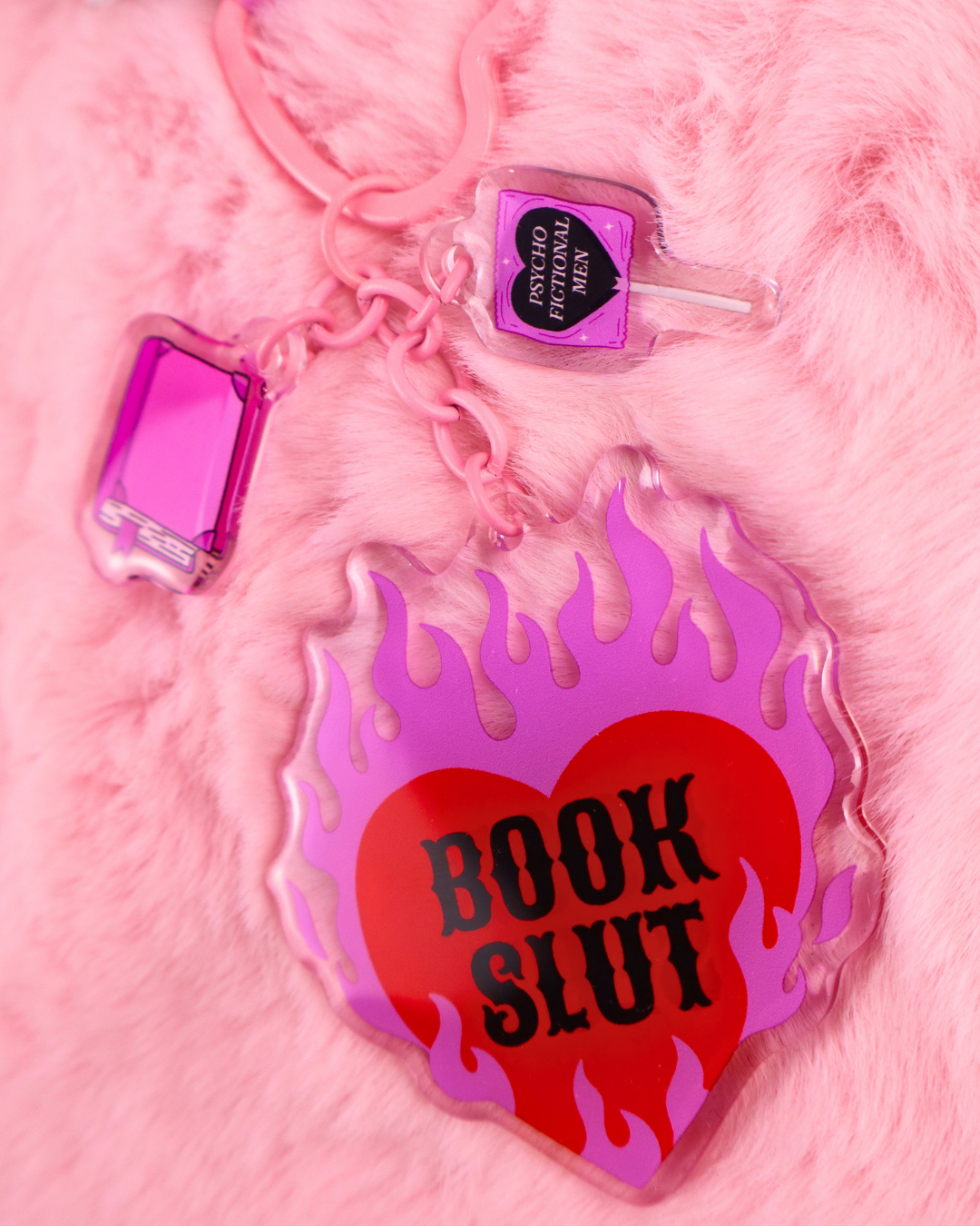 Pink Book Slut keychain with heart-shaped hardware and three bookish charms, a funny book lover accessory for bags, keys and book sleeves.