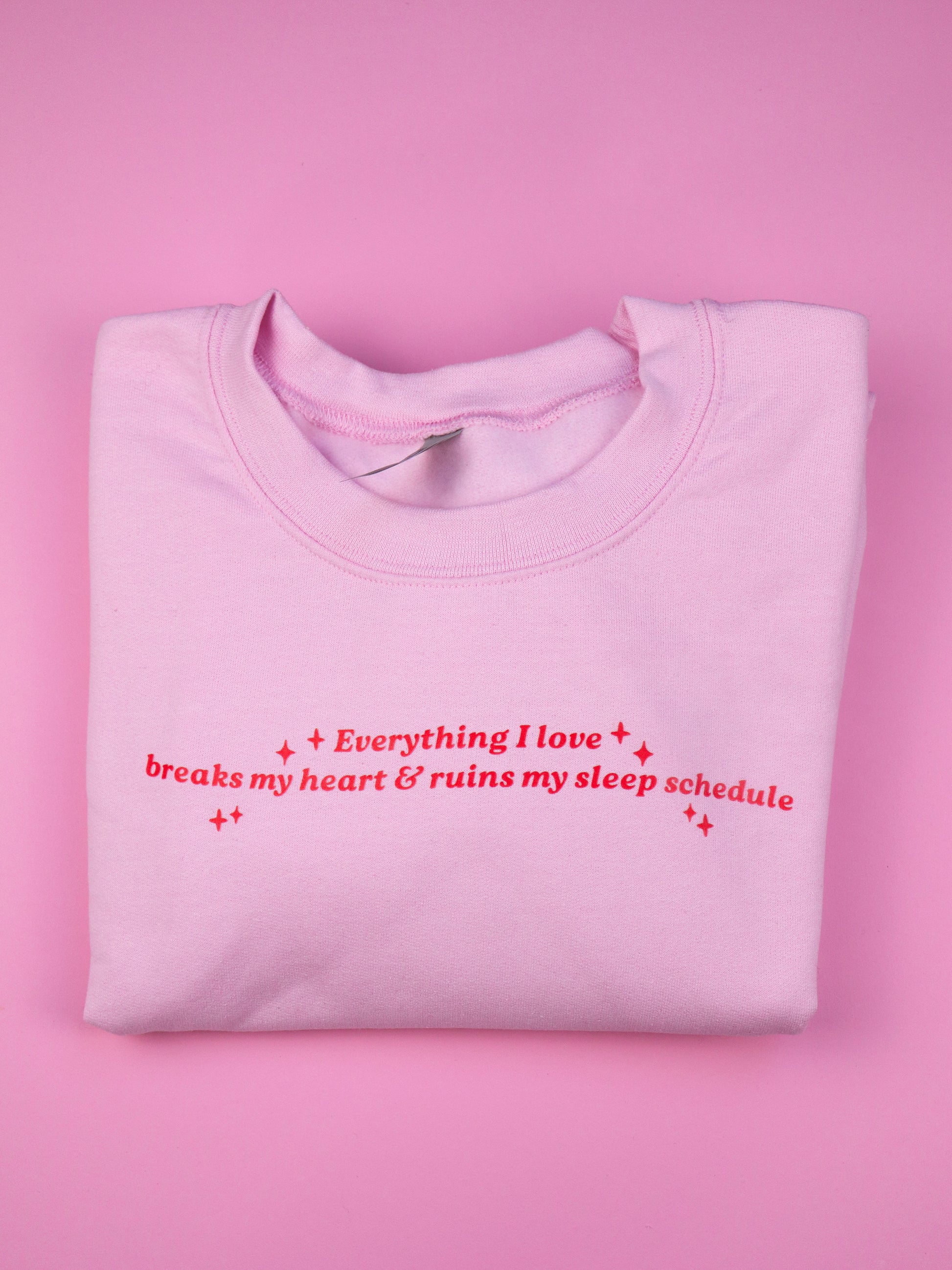 Folded pink sweatshirt with red text on a pink background, bookish sweater, crewneck, sweatshirt, heartbreak, romance reader, romantasy, dark romance themed sweater, bookish gift, apparel, booktok, book lover sweatshirt